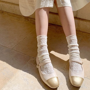 Close-up of off-white Mary Jane shoes with gold toe caps and white lace floral socks