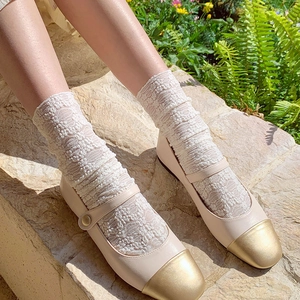 Close-up of beige Mary Jane flats with gold cap toe and white lace socks on stone steps