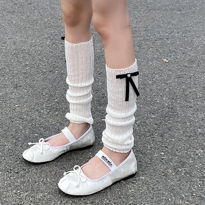 Close-up of white ribbed leg warmers with bows and satin ballet flats in balletcore style