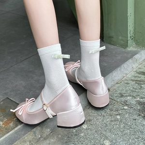 Close-up of pink satin Mary Jane pumps with bow detail and block heel on a model