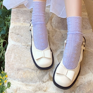 Close-up of off-white Mary Jane shoes with bow and floral lace socks on stone floor