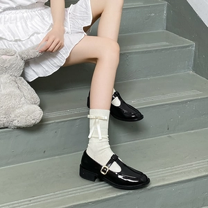 Détail de chaussettes blanches à nœuds en soie et chaussures Mary Jane noires