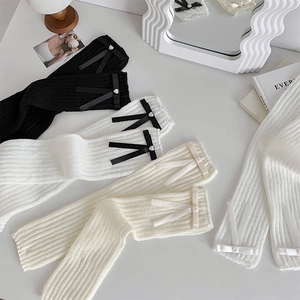 Close-up of knit leg warmers with satin bows and heart pearl charms in three colors