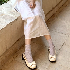 Close-up of cream Mary Jane mid-heel shoes with leather bows and lace socks on stone steps