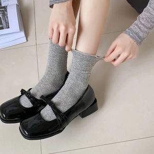 Women's black patent leather Mary Jane shoes with double bow straps and grey knit socks