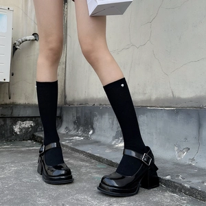 Detail of black platform Mary Jane shoes with silver heart buckle on knee-high socks
