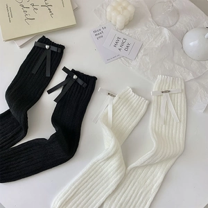 Detail view of leg warmers featuring satin bows and pearl accents on knitted fabric