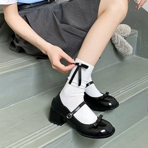 Gros plan de chaussures Mary Jane en cuir verni noir avec nœuds et chaussettes blanches