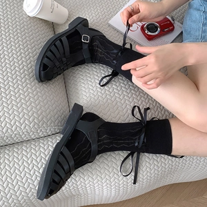 Detail of white mesh ballet socks with ribbon bows paired with black woven sandals