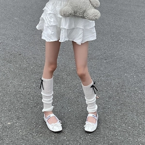 Close-up of white knit leg warmers with black bows and ballet flat shoes with straps