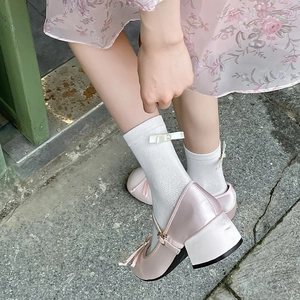 Close-up of pink satin Mary Jane heels and white mesh socks with delicate ribbon bows