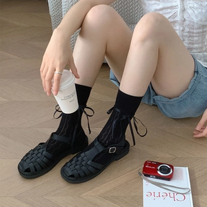 Detail of white mesh socks with ribbon bows and black woven sandals on wood floor