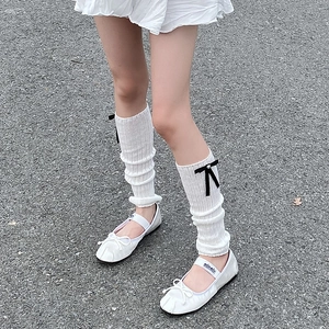Detail of white knit leg warmers with black silk bows and ballet flats on asphalt