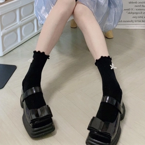 Detail of black platform loafers with bows and white bow-accented black ruffle socks