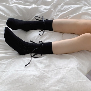 Close-up of black mesh socks featuring elegant silk bow details and wavy knit pattern