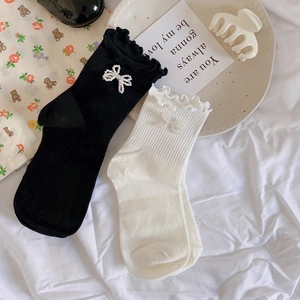 Detail of white and black mid-calf socks with pearl bows and ruffled edges on fabric