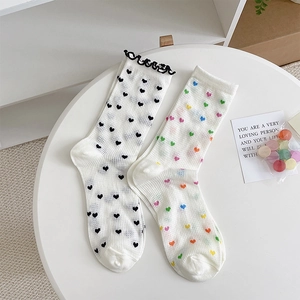 Detail view of white mesh crew socks with black heart patterns and ruffled cuffs