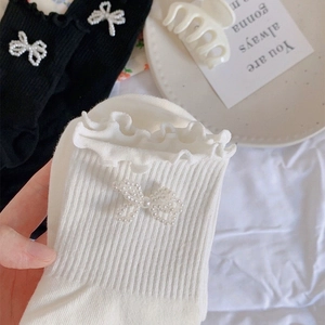 Close-up of knit calf socks with lace trim and elegant pearl bow accents in black and white