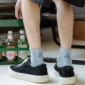 Detail of light blue ribbed socks with Save Money embroidery and black suede sneakers