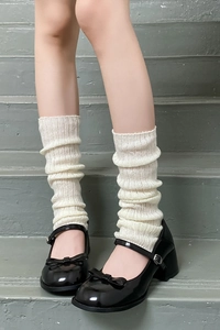 Close-up of off-white ribbed knit leg warmers paired with black Mary Jane shoes