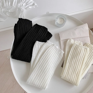 Detail of ribbed knit leg warmers in black, white, and beige on a minimal tray