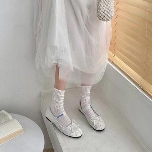 Close-up of white ballet flats with bow and mesh ruffle socks in a soft aesthetic room