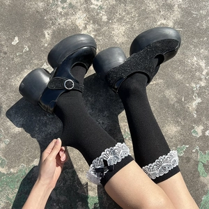 Détail de chaussettes hautes Lolita noires avec dentelle blanche et nœuds décoratifs