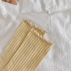 Detail of light yellow rib-knit socks featuring delicate ruffle edges and soft texture
