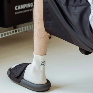 Close-up of white cotton sports socks with Save Money embroidery and black sandals