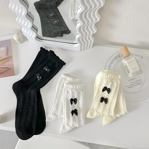 Détail de chaussettes à volants tricotées avec nœuds en satin noir, blanc et crème