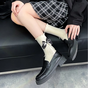 Detail of cream lace socks with black bows paired with glossy platform loafers