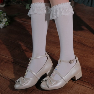 Detail of beige Lolita platform shoes with bows, pearls and crystals on wooden floor