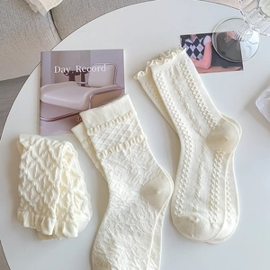 Detail of three cream knit socks with floral, diamond, and vertical cable patterns