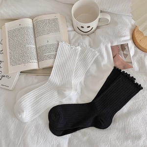 Flat lay of cotton knit crew socks with lettuce trim and ribbed texture on white bedding