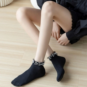 Black crew socks with lace ruffles and pearl beads on light wood background