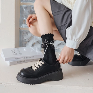 Close-up of black Lolita platform shoes with white lace bow socks on a white stair step