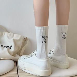 Detail of white ribbed mid-calf socks with 'TRYING MY BEST' text and canvas shoes