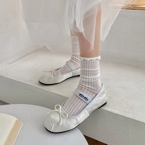 Detail of white ballet flats with bow and sheer mesh socks in minimalist white setting
