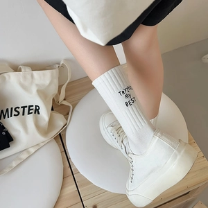 Detail view of white mid-calf socks with vertical rib knit and black slogan embroidery