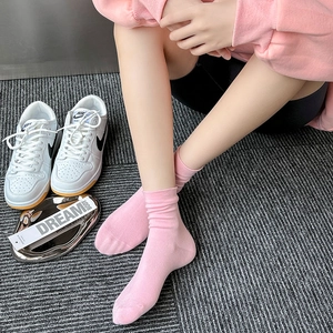 Detailed view of pink cotton slouch socks styled with white sneakers on a grey rug