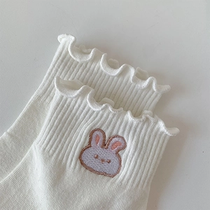 Détail de chaussettes blanches à volants avec broderie lapin et texture côtelée