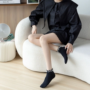 Close-up of black ribbed socks with white pearls and elegant lace trim detailing