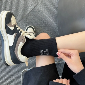 Detail of black ribbed mid-calf socks with white embroidery and retro sneakers