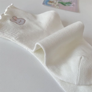 Détail de chaussettes blanches à volants avec broderie lapin et bords ondulés