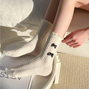 Détail de chaussettes montantes blanc crème avec bordure dentelle et nœuds noirs