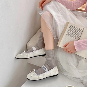 Detail of white ballet flats with bow and elastic logo strap paired with mesh socks