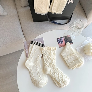 Close-up of three cream-white crew socks featuring cable knit patterns and ruffled lace cuffs