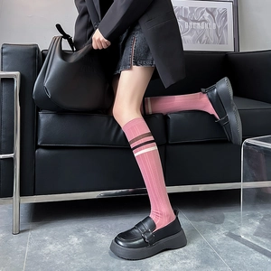Detail of pink knee-high socks with striped cuffs shown on model in stylish black outfit