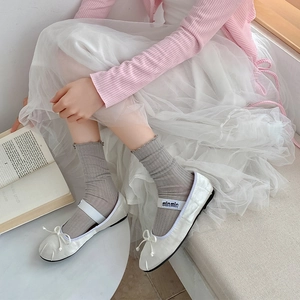 Detail of white Mary Jane ballet flats with mesh socks and ribbon bow on satin material