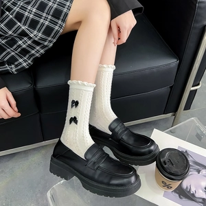 Détail de chaussettes mi-mollet en maille torsadée crème avec volants et nœuds noirs